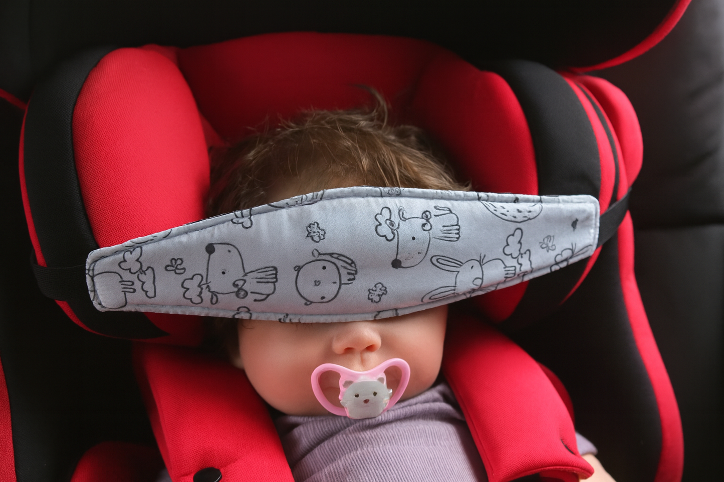 Baby in a red car seat with a sleep mask and pacifier