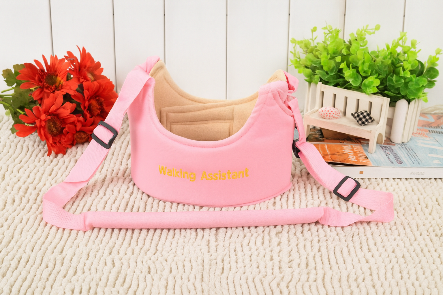 Pink 'walking assistant' harness on a textured surface with flowers and plants in the background